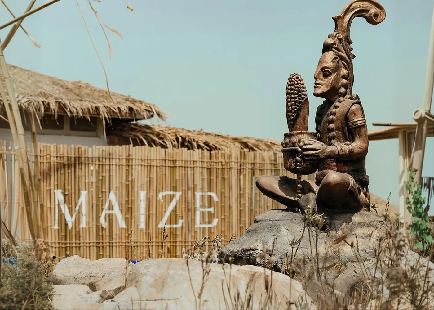 הכניסה: קיר קנים עם האותיות MAIZE ופסל של אל התירס עם קלח